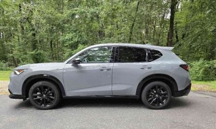 Silver 2025 Acura ADX A-Spec crossover with black wheels, parked on asphalt road surrounded by lush green forest trees
