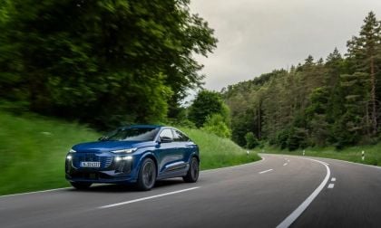 Blue Audi Q4 e-tron electric SUV driving on a winding forest highway in motion