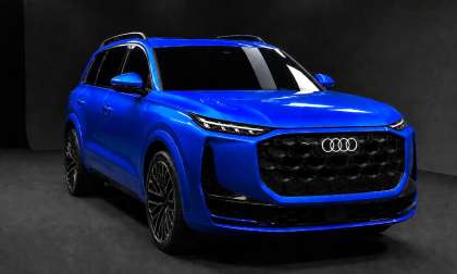 A blue Audi Q9 SUV shown from the front in a dark studio with illuminated Audi rings.