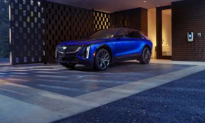 Blue Cadillac Lyriq parked under a modern carport next to a home EV charger.