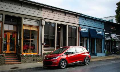 Red Chevrolet Bolt EV parked along a small-town street in front of storefronts.