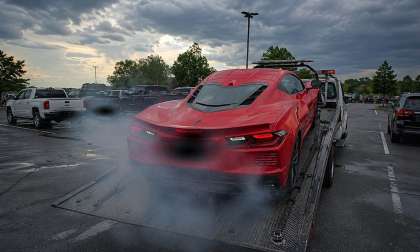 A red Chevrolet Corvette sits on a tow truck bed with smoke around the rear of the car.