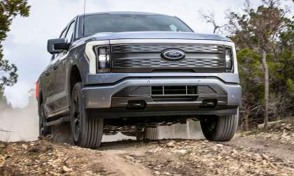 Ford F-150 Lightning Lariat driving off-road on a rocky dirt trail, shown from the front view.