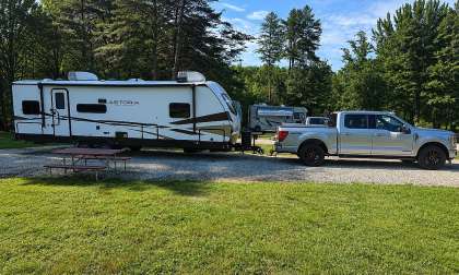 Ford F-150 pickup towing an Astoria travel trailer at a green campground site.