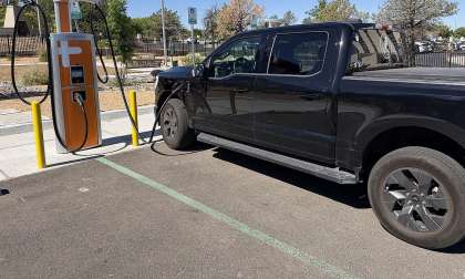 Black Ford F-150 Lightning charging at a ChargePoint station in a sunny parking lot.
