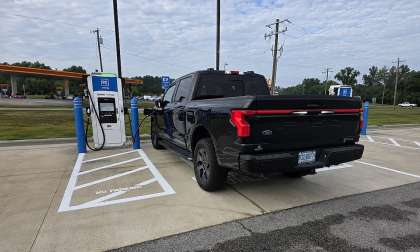 Black Ford F-150 Lightning charging at a GM Energy DC fast charger near a gas station.