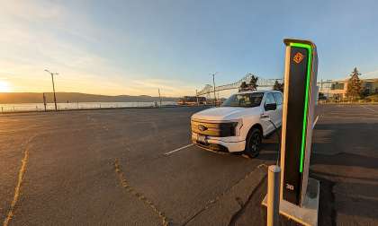 White Ford F-150 Lightning charging at a Rivian station near the waterfront at sunset.