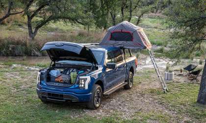 Blue Ford F-150 Lightning XLT set up at a campsite with an open frunk and rooftop tent.