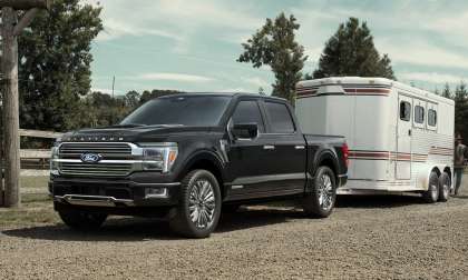 Black Ford F-150 Platinum towing a horse trailer at a ranch, with a person leading a horse alongside a wooden fence