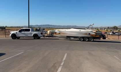 White Ford F-150 pickup towing a flame-graphic speedboat on a triple-axle trailer in a desert parking lot