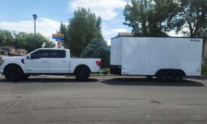 White Ford F-150 towing a large enclosed cargo trailer in a full side view on a residential street.