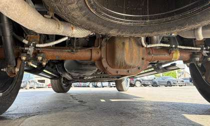 Close-up under a Ford F-150 XLT showing rust on the rear axle and differential while parked on a dealer lot.
