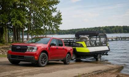 Red Ford Maverick pickup truck towing a Sea-Doo pontoon boat down a boat ramp into a lake