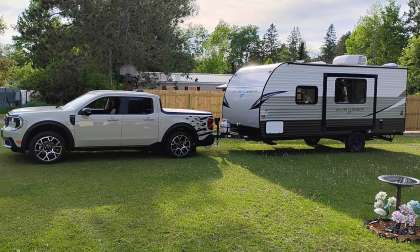 White Ford Maverick towing an Avenger LT camper trailer in a grassy yard.