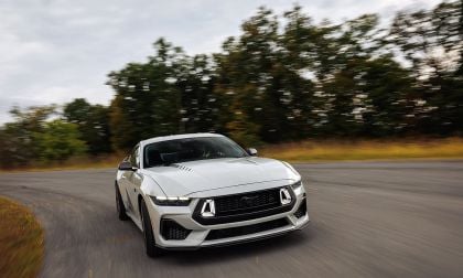 White Ford Mustang RTR driving head-on on autumn country road with motion blur trees in background
