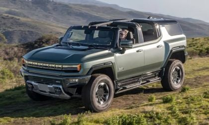 GMC Hummer EV white electric SUV driving on forest trail with evergreen trees