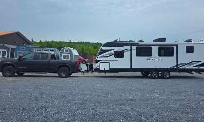 GMC Sierra AT4 HD towing an Imagine travel trailer in a side-profile view on a gravel lot.