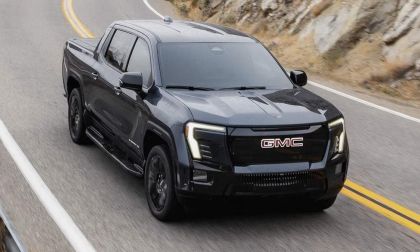 Black GMC Sierra EV electric pickup driving on a winding mountain highway, showcasing performance, LED lighting, and rugged design.