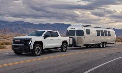 White GMC Sierra EV towing an Airstream travel trailer on a desert highway with mountains in the background.