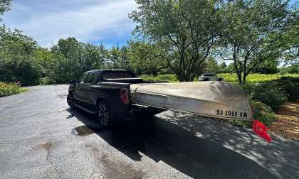 Black GMC Sierra EV towing a canoe on a small trailer in a residential driveway.
