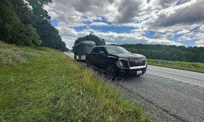 Black GMC Sierra EV parked on the roadside while towing a horse trailer under a cloudy sky.