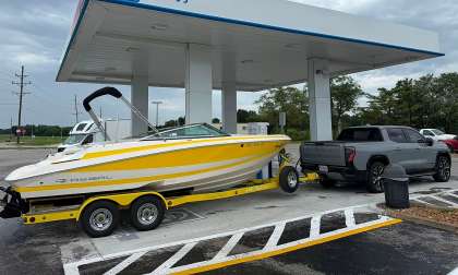 Gray GMC Sierra EV towing a yellow Regal boat while parked at a GM Energy charging station.