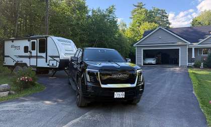 Black GMC Sierra EV parked in a driveway while towing a Winnebago Micro Minnie camper trailer.