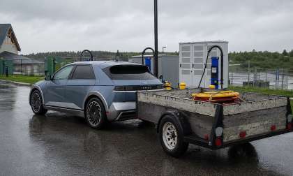Hyundai Ioniq 5 towing a utility trailer while parked near EV charging stations on a rainy day.