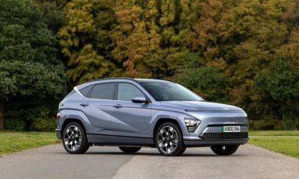 Grey Hyundai Kona Electric parked on a rural road at sunset, shown from a front three-quarter angle with a colorful sky.