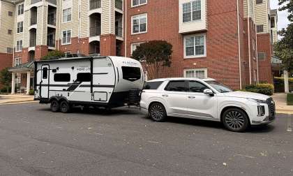 White Hyundai Palisade towing a Flagstaff Micro Lite travel trailer on a residential street.
