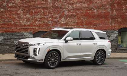 White Hyundai Palisade parked on a city street in a front three-quarter view near a brick wall.