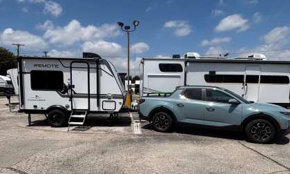 Light blue Hyundai SUV towing a white Coachmen Remote travel trailer at an RV dealership lot