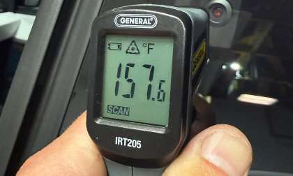 Infrared thermometer showing a 157.6-degree Fahrenheit temperature reading inside a vehicle.