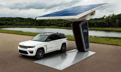 White Jeep Grand Cherokee 4xe plugged into a Jeep-branded charging station with a large solar canopy.