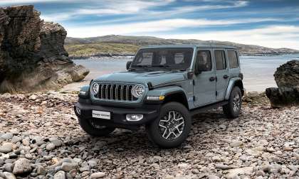Front three-quarter view of a Jeep Wrangler Unlimited 4xe on rocky terrain by the coast.