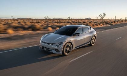 Silver Kia EV6 electric crossover cruising desert highway at sunset with Joshua trees in background