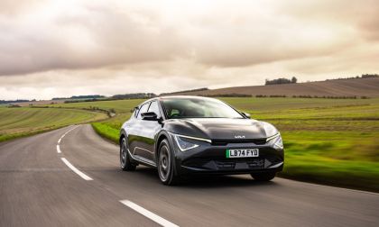 Kia EV6 electric crossover driving along a scenic rural highway under dramatic cloudy skies.