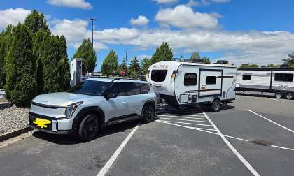 Kia EV9 towing a small travel trailer while parked at an EV charging station