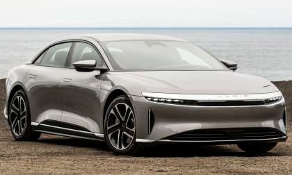Silver Lucid Air electric sedan parked on a dirt bluff overlooking the ocean, front three-quarter view showing signature light bar headlights
