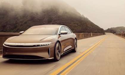 Image of a gold Lucid Air Dream Edition driving on a highway with a mountainside visible to the left hand side of the road.