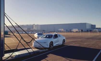 Image showing a Lucid Air wearing protective white wrapping being driven into a covered car transport trailer