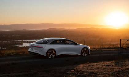 A white Lucid Air Grand Touring is parked on a hilltop at sunset.