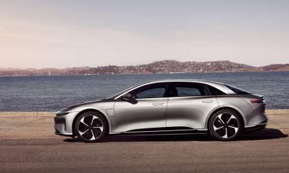 Side view of a silver Lucid Air parked on a waterfront with mountains visible in the distance.