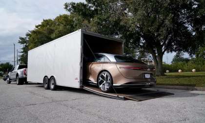 Image showing a gold Lucid Air being reversed out of an enclosed car trailer for customer delivery.