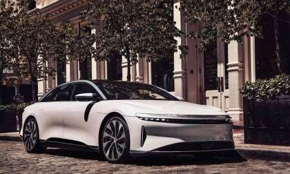 Image showing a Lucid Air with white paint parked in front of some trees.