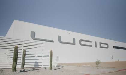 Image of the entrance to Lucid's AMP-1 factory. The white building and large silver Lucid logo contrast the blue desert sky,