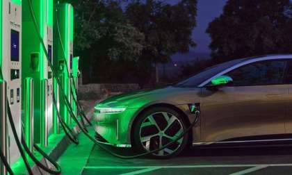 A gold Lucid Air Dream Edition is pictured plugged in at an Electrify America charging station bathed in a green glow.