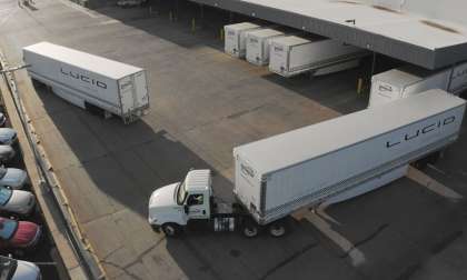 Image showing semi trucks with Lucid logos on their trailers pulling away from a loading depot.
