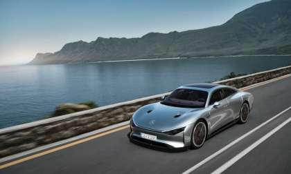 Image showing a rendering of a silver Mercedes-Benz EQXX concept car driving beside a lake with mountains in the background.
