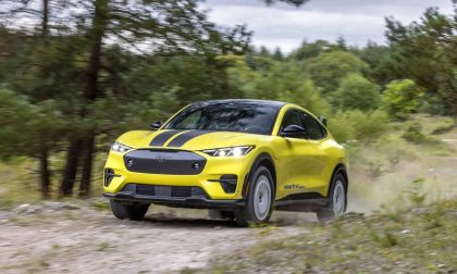Bright yellow Ford Mustang Mach-E Rally driving on dirt trail through forest